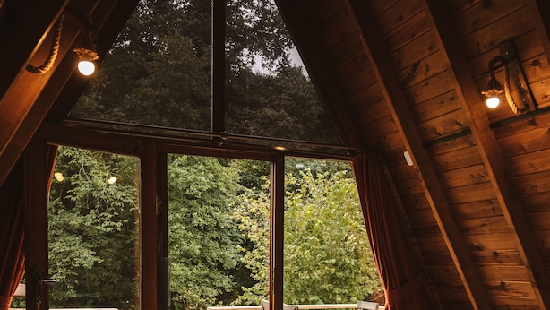 Un dormitorio acogedor en el ático con un amplio ventanal, techo de madera y vistas a un jardín exuberante.