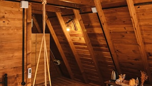 Un dormitorio de buhardilla con piso de madera, una cama, un refrigerador pequeño y una lámpara colgante.