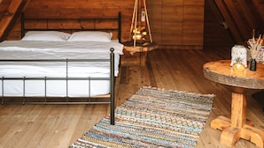 Acogedor dormitorio en ático con techo de madera, una cama, lámpara colgante y una pequeña mesa con adornos.