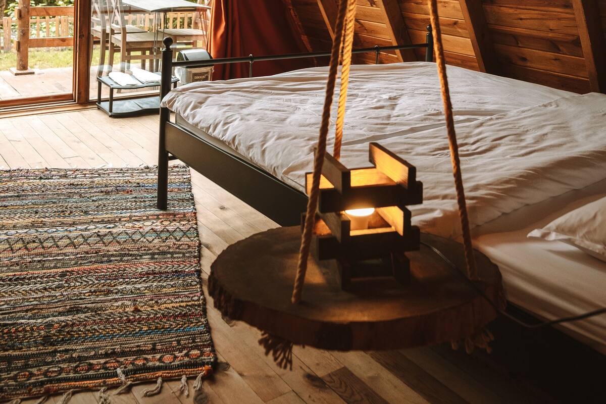 Ein Holzinnenraum mit einem Bett, einer Hängelampe und Blick ins Freie.
