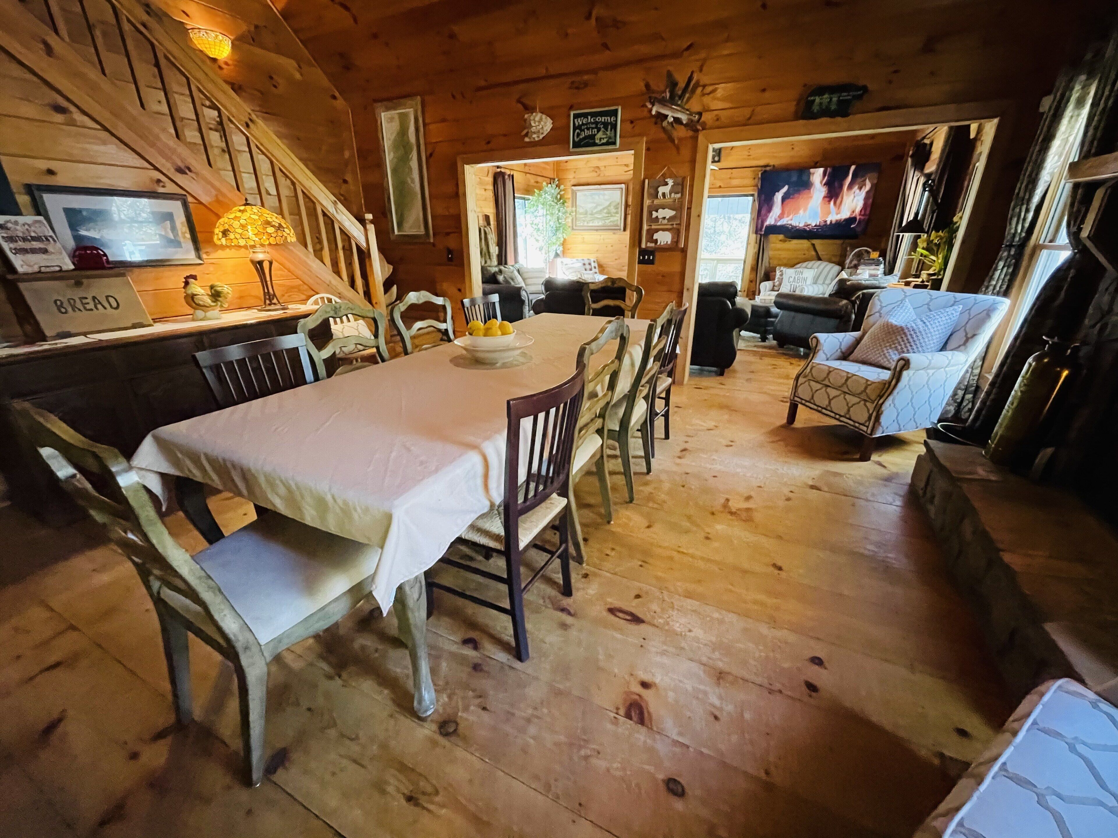 A wooden cabin interior with a dining area, a sofa, and a television.