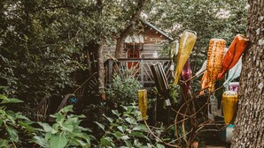 A rustic wooden cabin surrounded by dense foliage, with colorful glass bottles hanging from a tree. - The Treehouse, with a deck for grilling and relaxation. (Terrell)