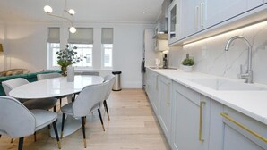 A modern kitchen with white cabinets, a marble countertop, and a stainless steel sink. There is a dining area with a round table and chairs. - 3 bedroom apartment in the heart of Kensington (London)