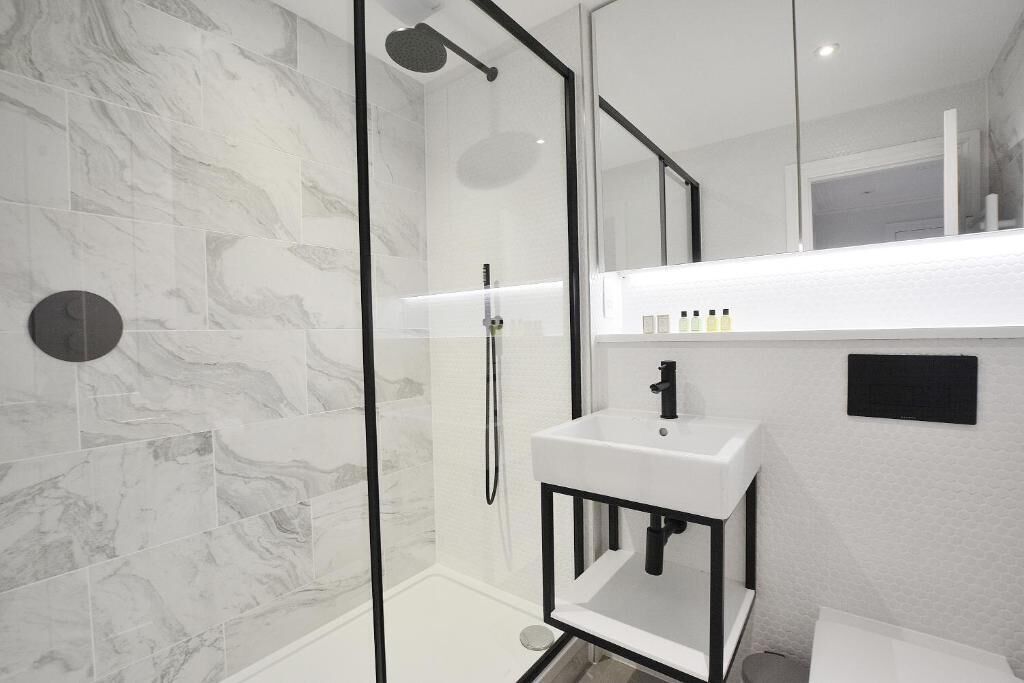 Une salle de bain moderne avec une douche à parois de verre, un lavabo blanc et un mur décoré d’un motif imitant le marbre.