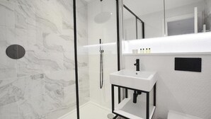 A modern bathroom with a glass-enclosed shower, a white sink, and a marble-patterned wall. - 3 bedroom apartment in the heart of Kensington (London)