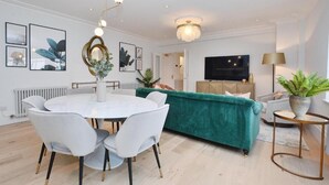 A modern living room with a round dining table, teal sofa, and a flat-screen TV. - 3 bedroom apartment in the heart of Kensington (London)