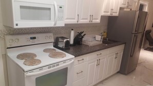 A kitchen with white cabinets, a microwave, a stove, a toaster, and a refrigerator.
