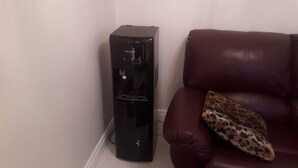A black water dispenser next to a brown leather couch with a leopard print pillow.