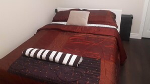 A neatly made bed with a red bedspread, a striped pillow, and a folded blanket.
