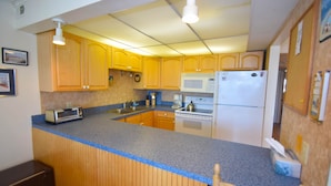 A compact kitchen with wooden cabinets, a built-in microwave, a refrigerator, and a toaster. - Thunder Island 80B-Baywater 39th St, Free WiFi, Pool, Elev, W/D, AC (Ocean City)