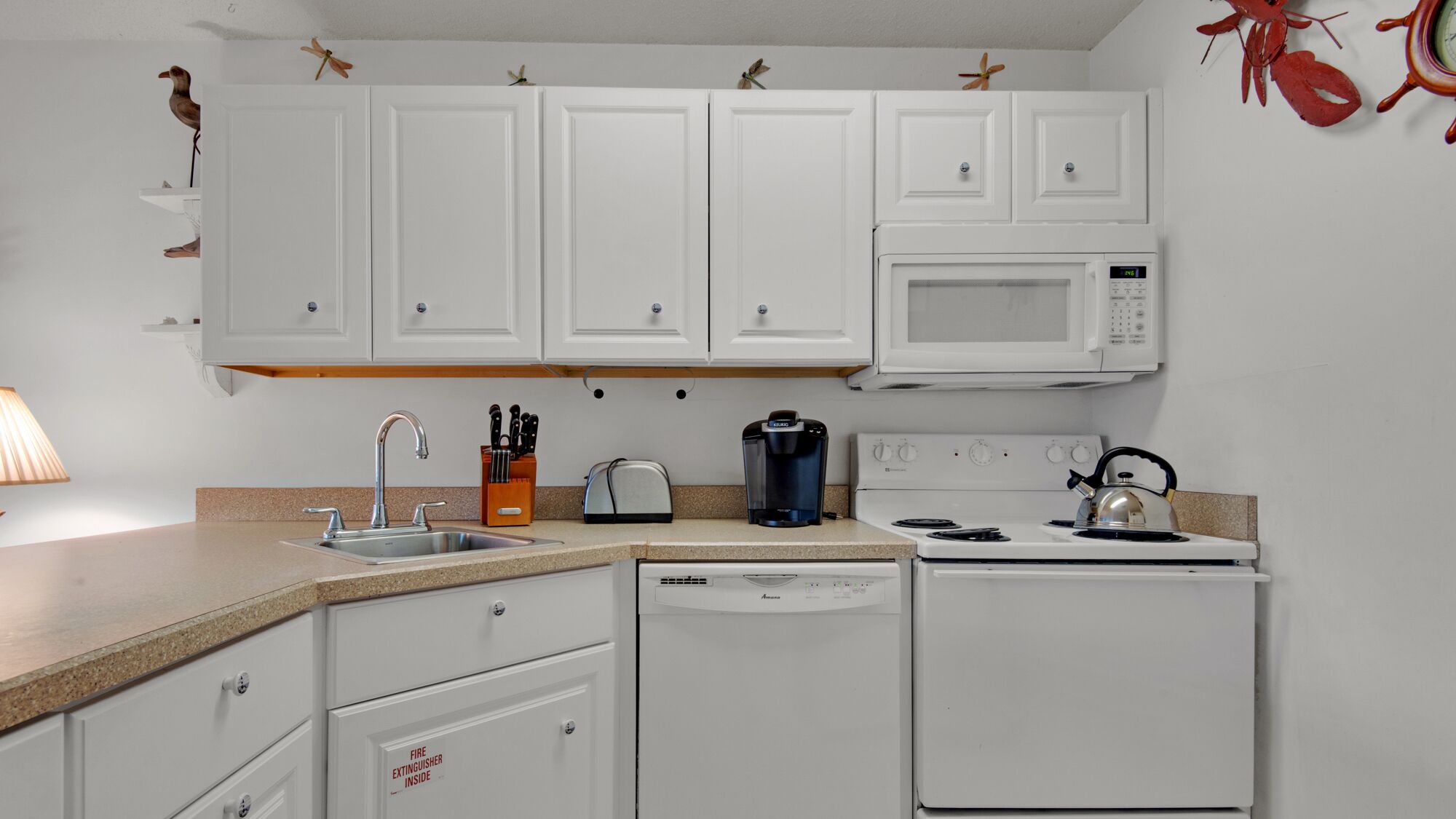 A kitchen with white cabinets, a microwave, a toaster, a coffee maker, a kettle, and a dishwasher.