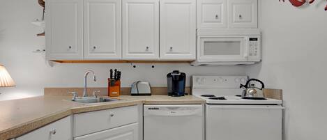 A kitchen with white cabinets, a microwave, a toaster, a coffee maker, a kettle, and a dishwasher.