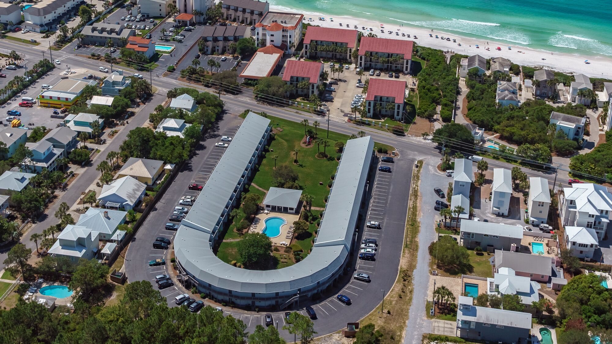 An aerial view of a coastal hotel with a curved building, a swimming pool, and a beach nearby.