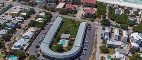 An aerial view of a coastal hotel with a curved building, a swimming pool, and a beach nearby.
