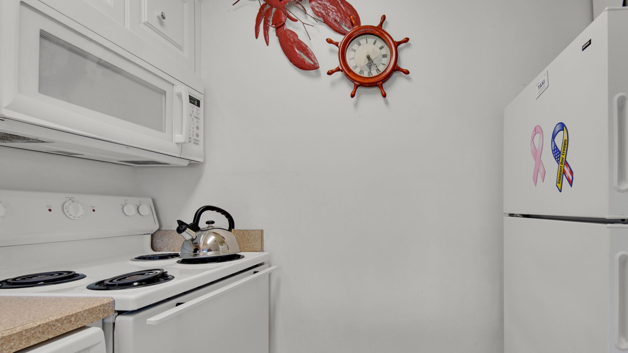 Una cocina con electrodomésticos blancos, un reloj rojo y una tetera sobre la estufa.