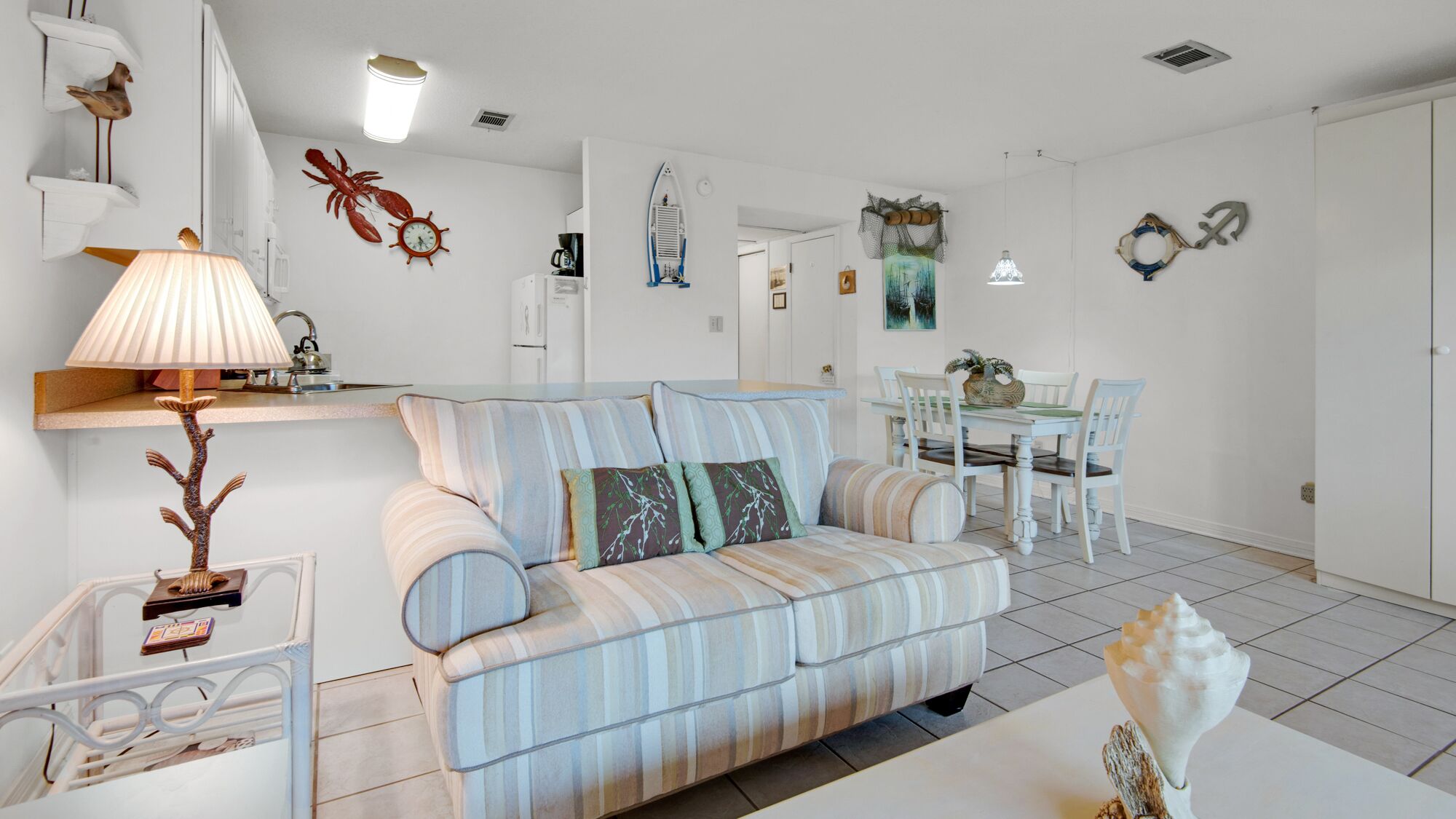 A modern living room with a striped sofa, a dining table with chairs, and a kitchen area with white cabinets.