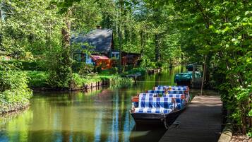 A riverside dock with a rowboat, a wooden walkway, and a house with a red roof.
