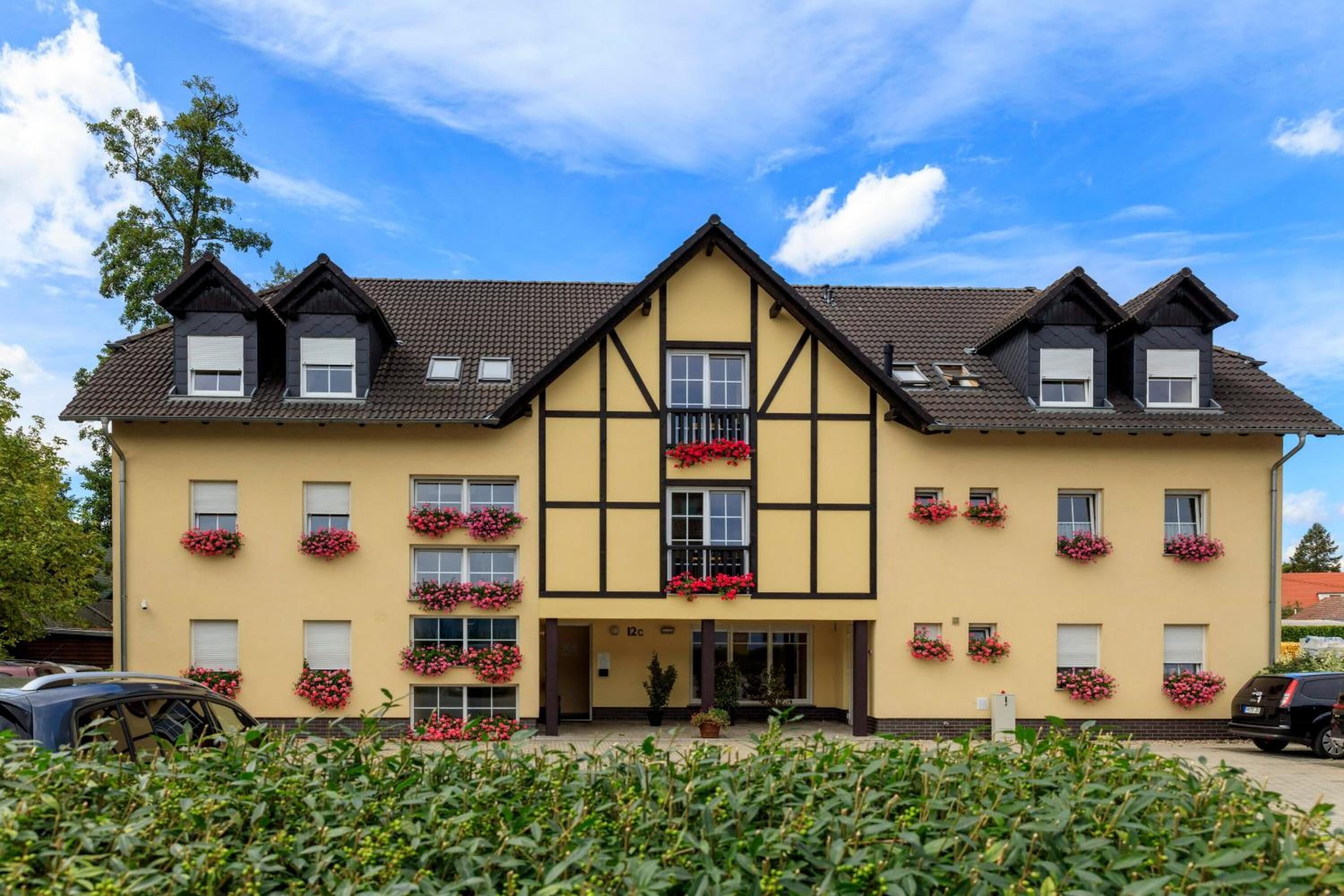 A two-story building with a symmetrical facade, multiple windows with flower boxes, and a central entrance.