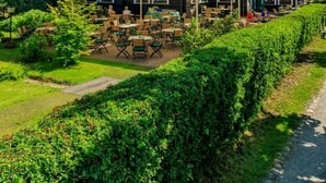 Een groot gebouw met een groen dak en een windmolen, terras met parasols en een verzorgde tuin.