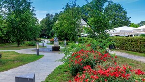 Een pad dat leidt naar een gebouw in traditionele stijl, omringd door weelderig groen en rode bloemen.