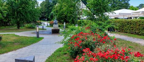 A pathway leading to a building with a traditional architectural style, surrounded by lush greenery and red flowers.