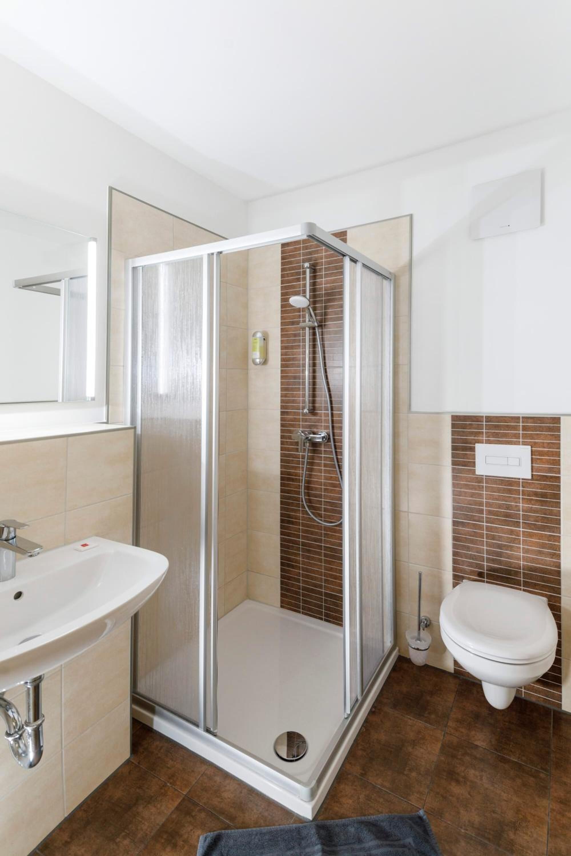 Un baño moderno con ducha envuelta en cristal, un lavabo blanco y un inodoro.