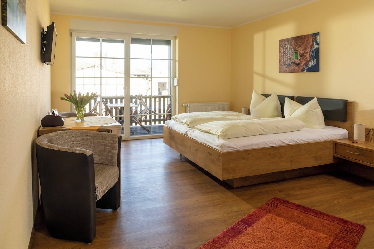 A bedroom with a bed, a chair, a desk, a window, and a door.