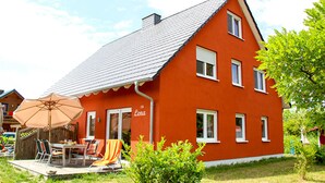 Une maison rouge avec un toit en pente, une terrasse avec des meubles d’extérieur et une enseigne sur laquelle on peut lire « Lena ».