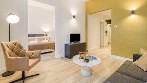Ein modernes Hotelzimmer mit einem Bett, einem Fernseher, einem runden Couchtisch und einer Sitzecke mit Sessel und Sofa.