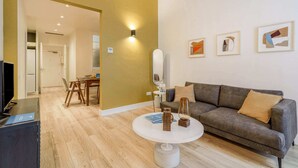 Ein modernes Wohnzimmer mit einem grauen Sofa, einem runden Couchtisch und einem Essbereich mit Tisch und Stühlen.