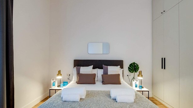 A bedroom with a bed, two bedside tables, a nightstand, a mirror, and a wardrobe. - Sweett | Sepulveda Principal A (Barcelona)