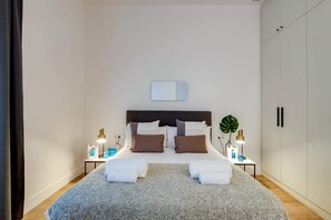 Un dormitorio con una cama, dos mesitas de noche, un tocador, un espejo y un armario.
