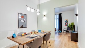 A modern dining area with a wooden table, grey upholstered chairs, and a contemporary light fixture. - Sweett | Sepulveda Principal A (Barcelona)