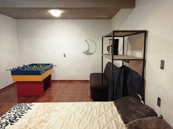 A room with a bed, a foosball table, a chair, and a shelf with a coffee machine.