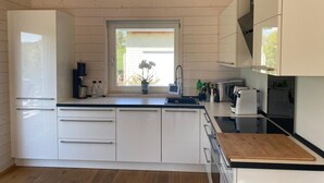 Moderni keittiö, jossa on valkoiset kaapit, puinen työtaso ja ikkuna, josta avautuu näkymä vehreään maisemaan.