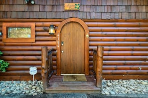 Une cabane en rondins de bois, dotée d’une grande porte en arc de cercle, d’une petite fenêtre et d’une enseigne indiquant « Alpine Rose ».