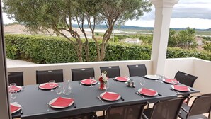 A dining table set for six with red napkins, glasses, and a vase of flowers. The table is outdoors with a view of a vineyard and hills. - 5 minutes from the beaches , Villa with  Pool, Boulodrome, Pinball and Babyfoot (Vendres)