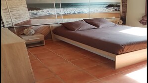 A bedroom with a large window, a bed with brown bedding, a bedside table, and a woven wall decoration. - 5 minutes from the beaches , Villa with  Pool, Boulodrome, Pinball and Babyfoot (Vendres)