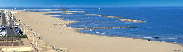 Una playa con un largo paseo marítimo, cielo despejado y el texto "VALRAS-Plage" que indica la ubicación.