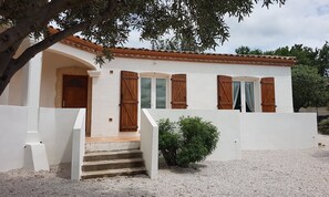 A white building with a tiled roof, wooden shutters, and a small staircase leading to the entrance.