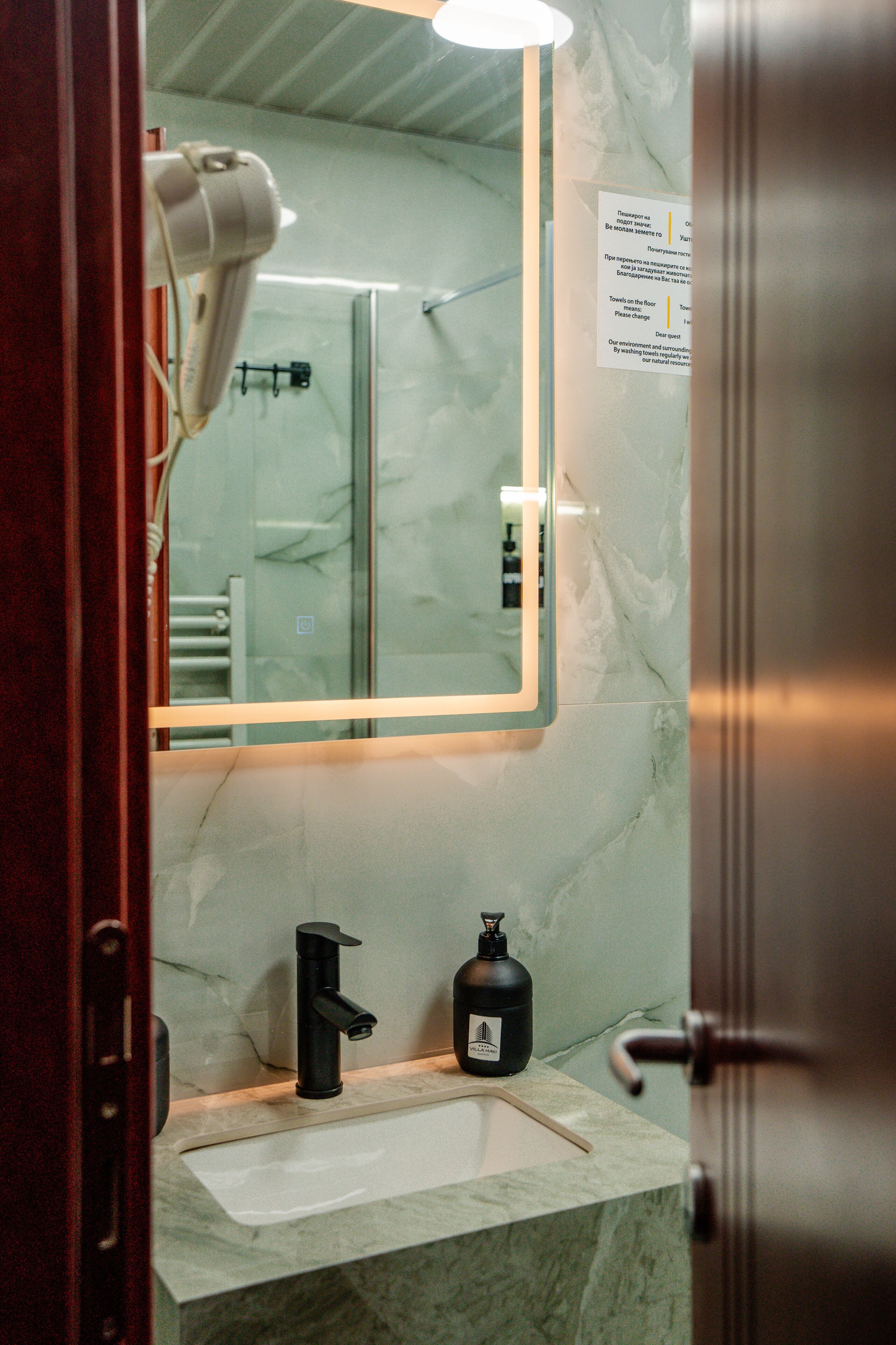 A bathroom with a marble sink, a black soap dispenser, and a hairdryer on the wall.