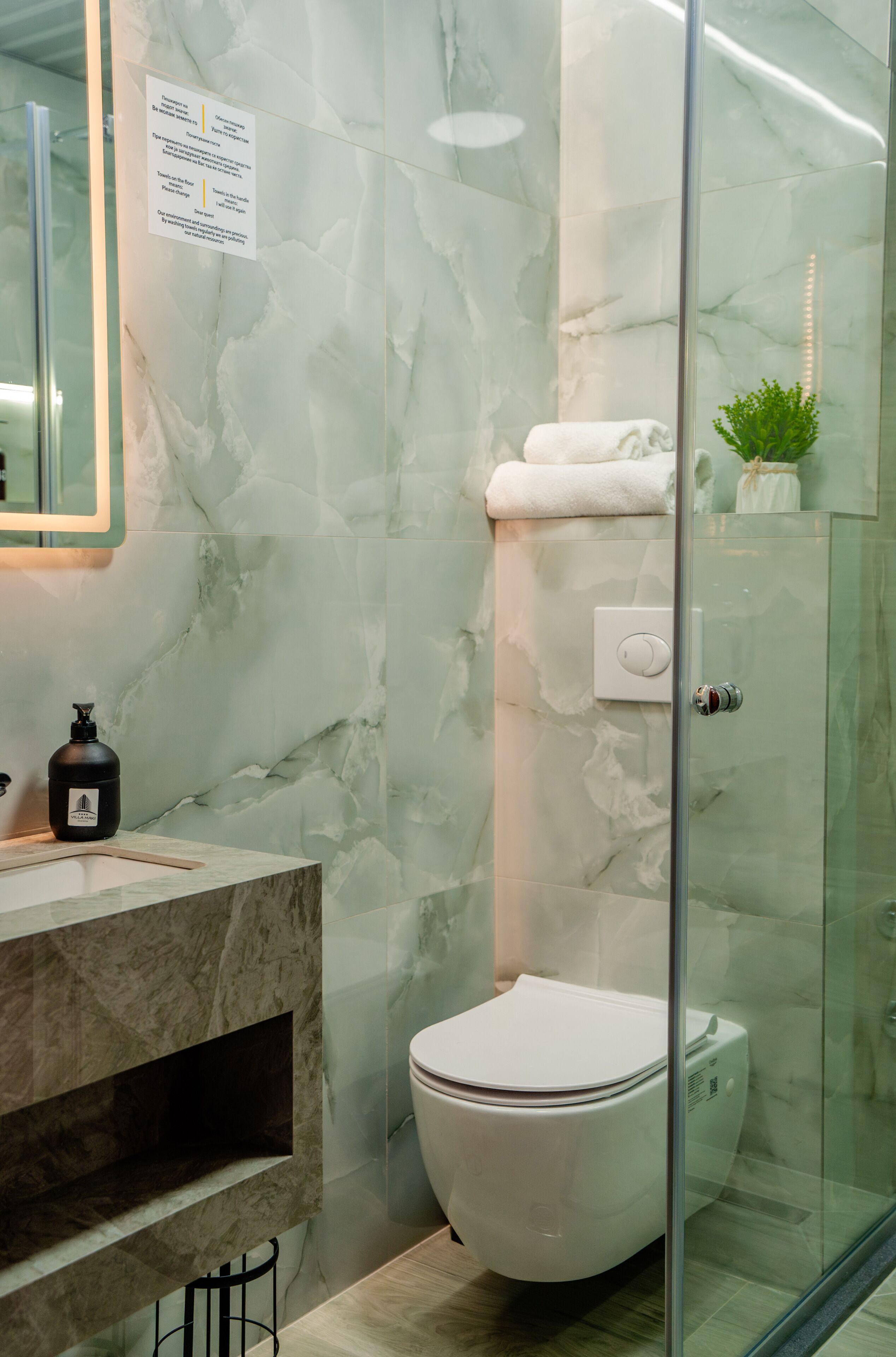 Un baño moderno con cabina de ducha de vidrio, pared de mármol, inodoro blanco y lavamanos con encimera de mármol.