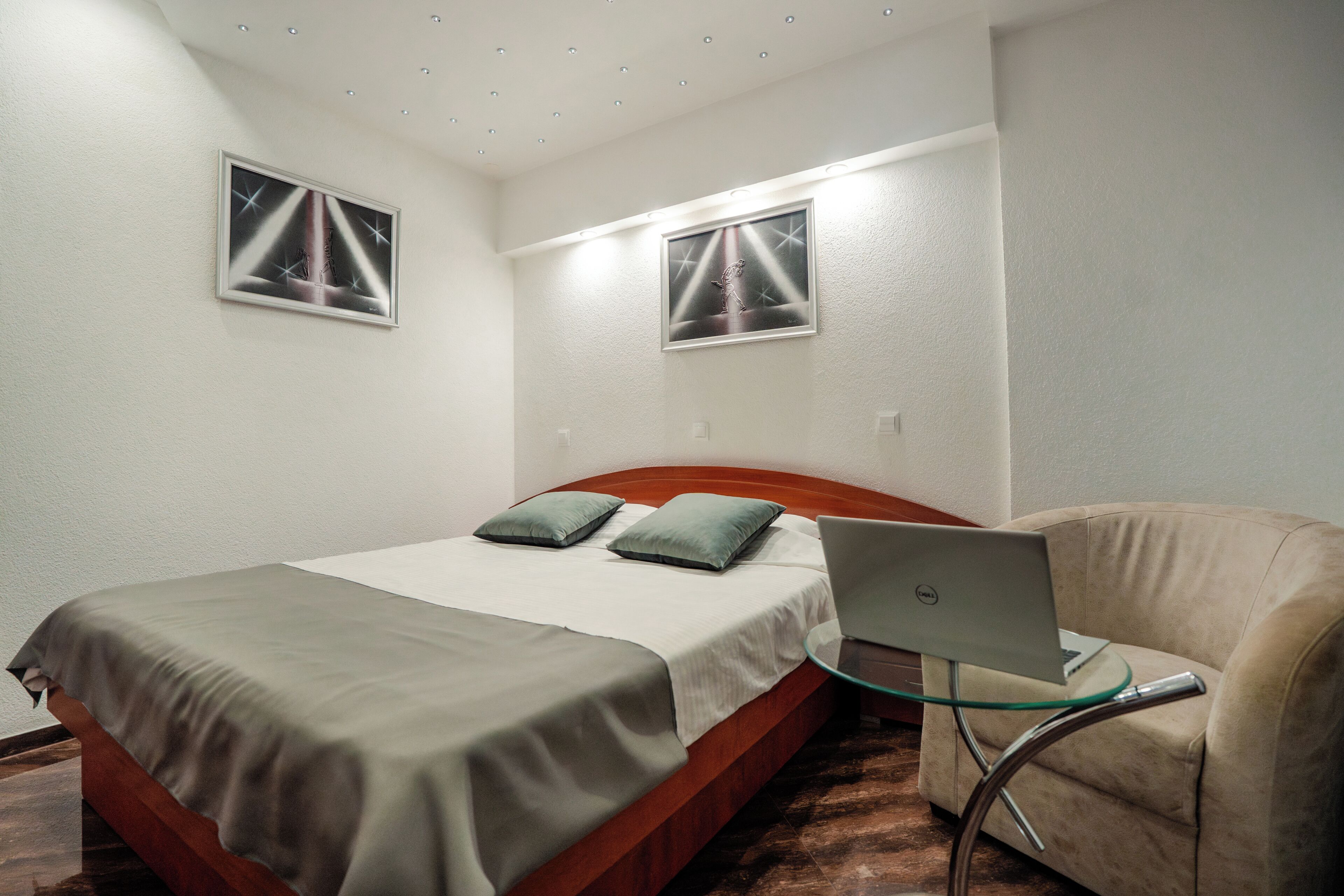 A hotel room with a bed, a laptop on a glass table, and two framed pictures on the wall.