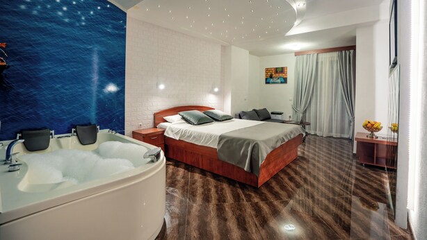 Quarto de hotel moderno com uma cama grande, banheiro separado com banheira, escrivaninha com cadeira e uma janela ampla com cortinas.