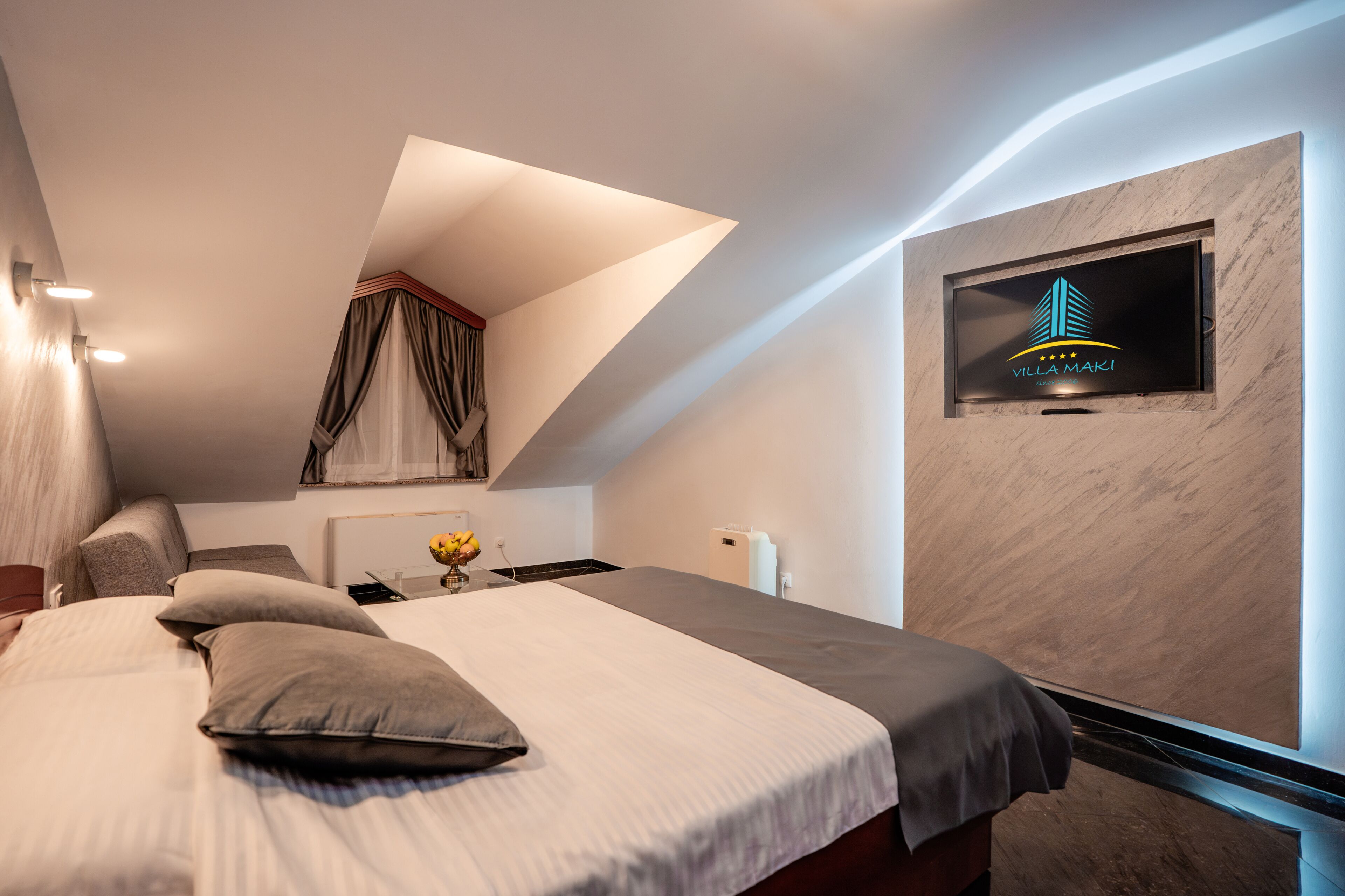 Une chambre d’hôtel moderne équipée d’un lit, d’un bureau, d’une chaise, d’un téléviseur fixé au mur et d’une fenêtre avec des rideaux.