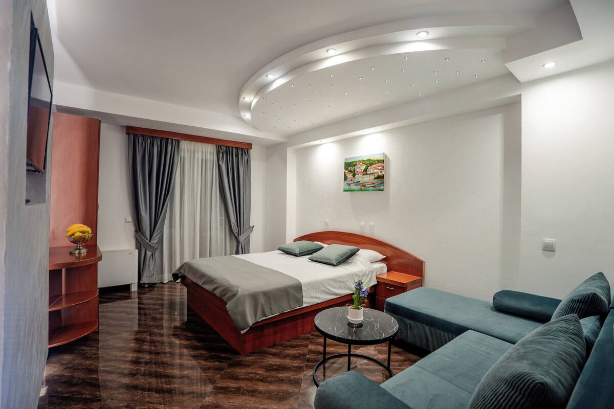 A hotel room with a bed, a sofa, a small table, and a painting on the wall.