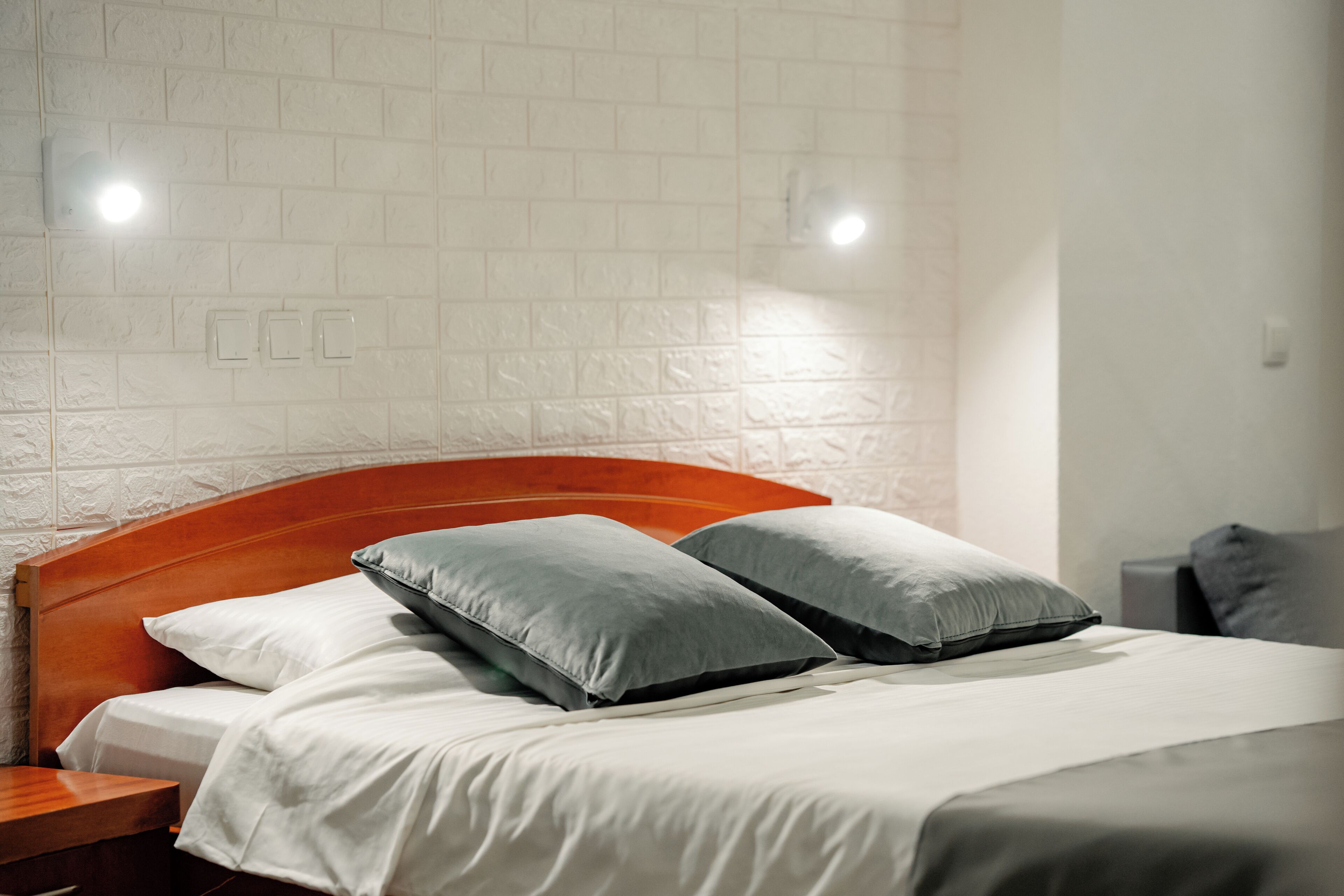 A neatly made bed with a wooden headboard, two pillows, and a white wall with a textured pattern.