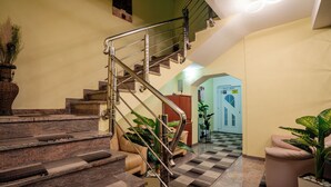 Uma escadaria com grades de metal, piso xadrez e plantas em vasos.