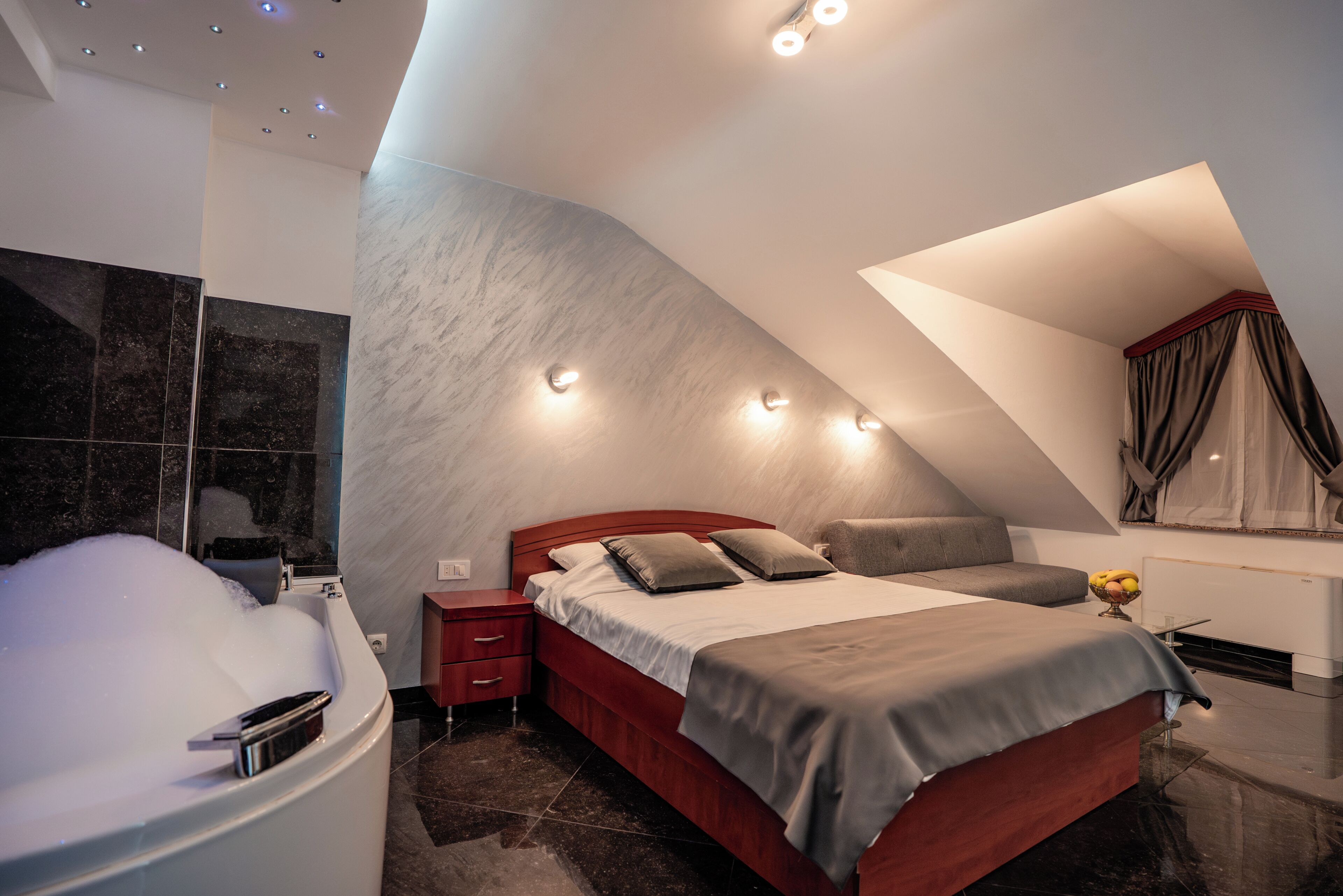 A modern bedroom with a curved ceiling, a large bed, a bathtub, and a small seating area.
