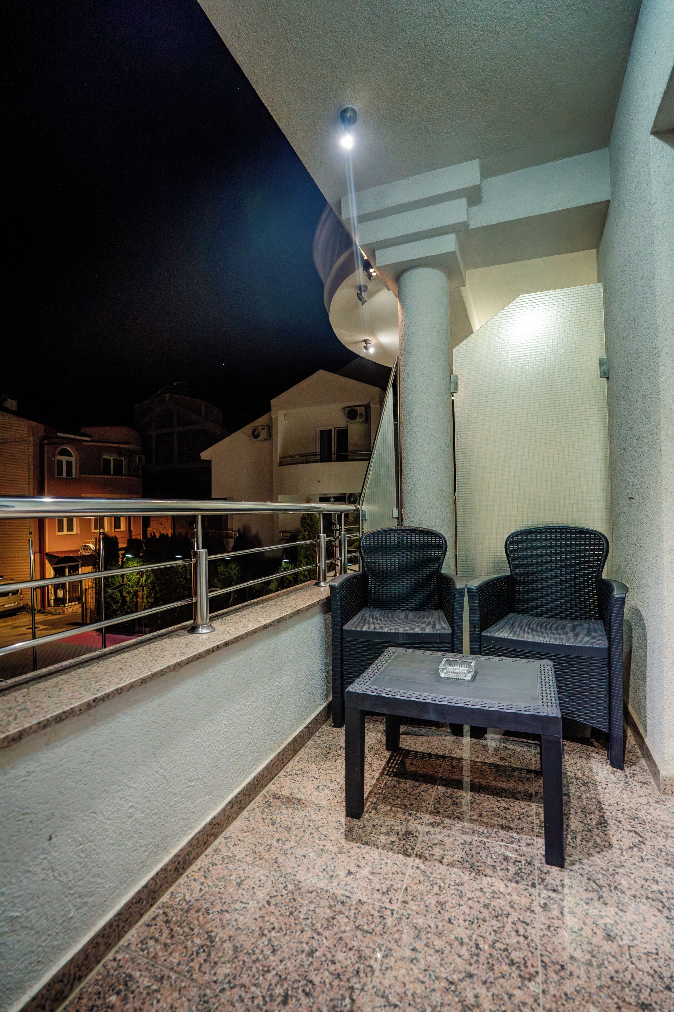 A balcony with two wicker chairs, a small table, and a railing.